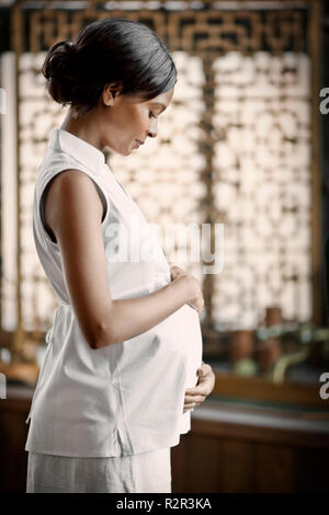 Pregnant young woman standing with her hand on her belly. Stock Photo