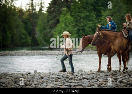 Mid-adult woman walking beside her two teenage daughters on horses. Stock Photo