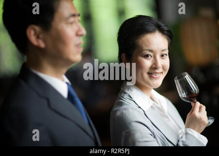 Portrait of a smiling young businesswoman standing next to a colleague while holding a glass of red wine. Stock Photo
