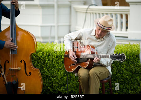 Young adult man sitting playing an acoustic guitar beside a man playing a cello. Stock Photo