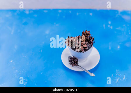 Christmas or new year concept. Composition with dried brown pinecone. Perfect for pattern fills, web page background, wallpaper, gift paper. Flat lay.pine cone in white cup on blue background for Christmas decorative. Stock Photo
