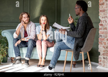 Young serious couple visiting a psychologist sitting on the comfortable Young serious couple visiting a psychologist sitting on the comfortable