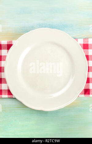 An overhead photo of a white plate on a gingham cloth on a teal blue wooden background with copy space Stock Photo