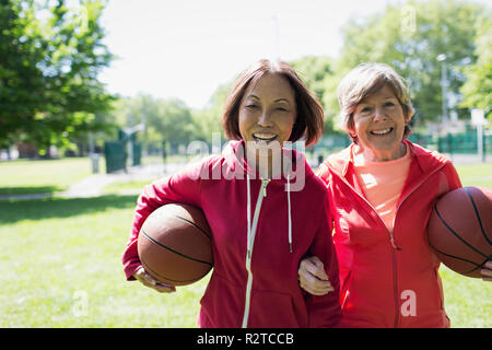 Portrait happy, active senior women friends playing basketball in sunny park Stock Photo