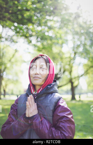 Serene active senior woman meditating in sunny park Stock Photo