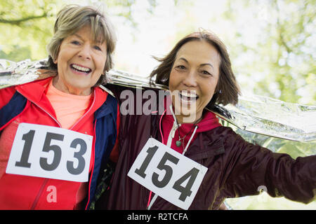 Portrait smiling, confident active senior women finishing sports race, wrapped in thermal blanket Stock Photo