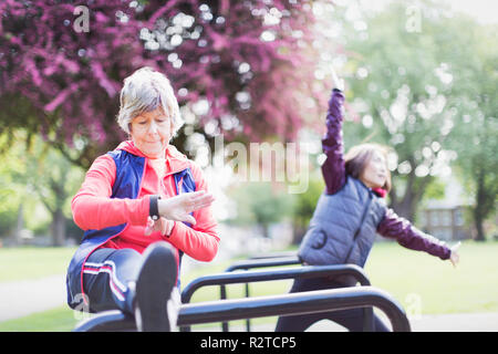 Active senior female runner stretching leg and checking smart watch Stock Photo