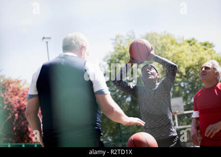 Active senior men playing basketball in sunny park Stock Photo