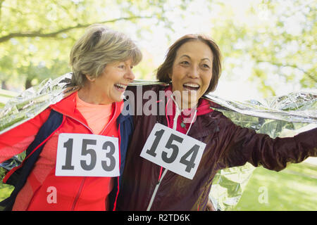 Happy active senior women finishing sports race, wrapped in thermal blanket Stock Photo