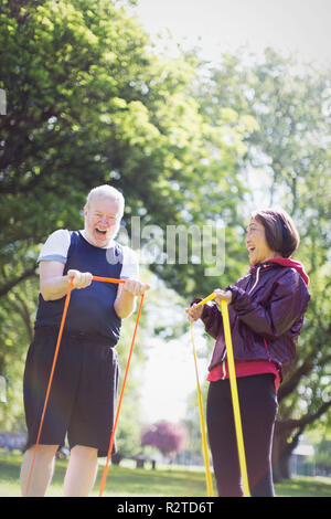 Enthusiastic active senior couple exercising, using resistance bands in sunny park Stock Photo
