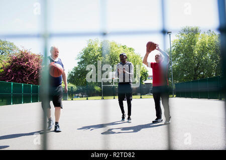 Active senior men playing basketball in sunny park Stock Photo