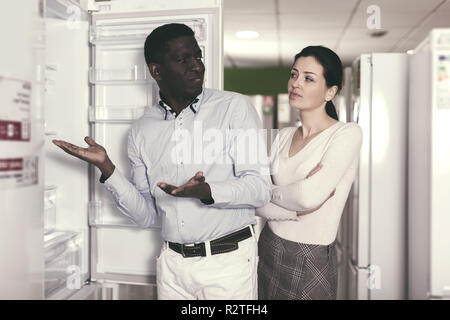 positive couple choosing fridge in store of household appliances Stock Photo
