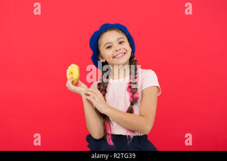 Sweets shop and bakery concept. Kids huge fans of baked donuts. Impossible to resist fresh made donut. Girl hold glazed cute donut in hand red background. Kid smiling girl ready to eat donut. Stock Photo