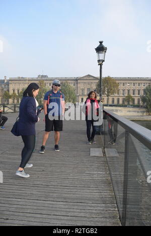 Peoples on Pont des Arts footbridge on the Seine River and People walking across a pedestrian bridge over the River Seine facing the Louvre museum Stock Photo