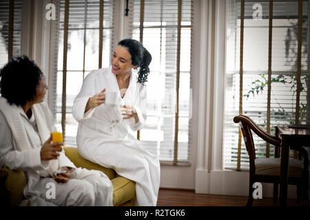 Two friends in bathrobes relaxing with morning drinks Stock Photo