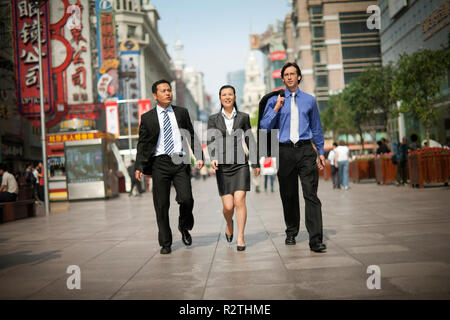 Three business colleagues walking down a busy street while talking. Stock Photo