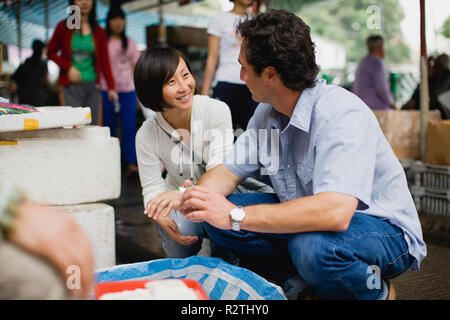 Young man and woman crouching next to a basket of merchandise in a market place in the city. Stock Photo