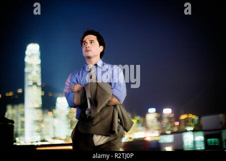 Serious young businessman standing outdoors in the city at night with his arms crossed. Stock Photo