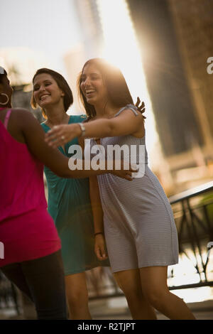 Two smiling friends reaching their arms out to hug another friend in the city. Stock Photo