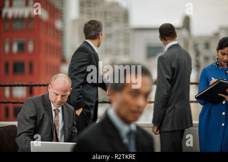 Mature businessman works on his laptop on the balcony of a high-rise corporate building. Stock Photo