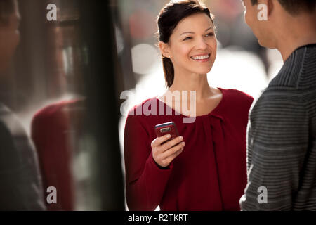 Smiling young woman holds her phone while talking with a friend. Stock Photo