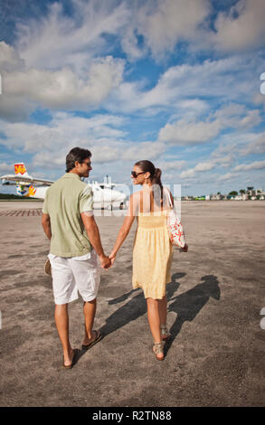 Smiling young married couple walking hand in hand toward an airplane. Stock Photo