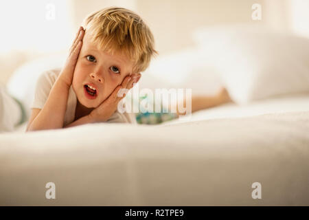 Young boy lying on his front puts his hands on his cheeks and makes a face as he poses for a portrait. Stock Photo