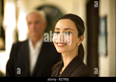Young businesswoman smiles as she poses for a portrait on a stone porch with a male colleague in the background. Stock Photo