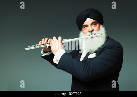 Well-dressed senior man in turban playing flute Stock Photo
