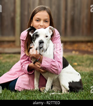 Portrait of pre-teen girl sitting on lawn hugging dog. Stock Photo