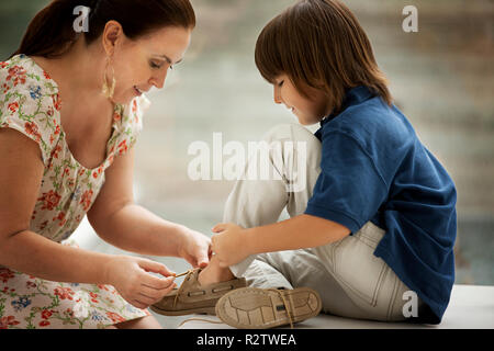 Middle-Aged mother helps her young son to tie his shoelaces. Stock Photo
