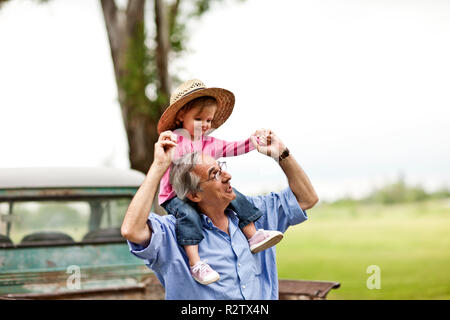 Mature man giving his toddler granddaughter a shoulder ride. Stock Photo