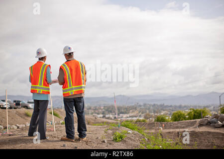 Two engineers in high visibility vests and hardhats discuss building plans on a construction site. Stock Photo