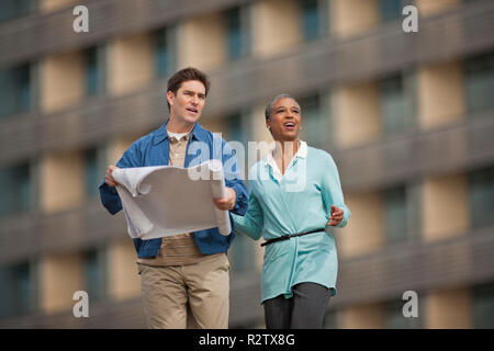 Two young engineers discussing building plans at a construction site. Stock Photo
