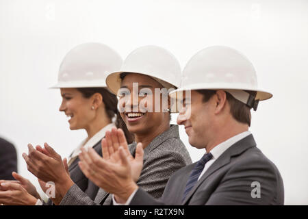Three smiling colleagues in business suits and hardhats applaud after the ground-breaking ceremony for a new building development. Stock Photo