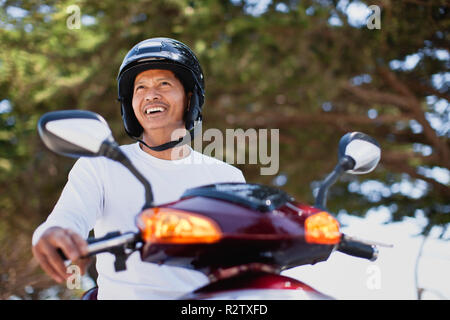 Man happily sitting on scooter with helmet on. Stock Photo