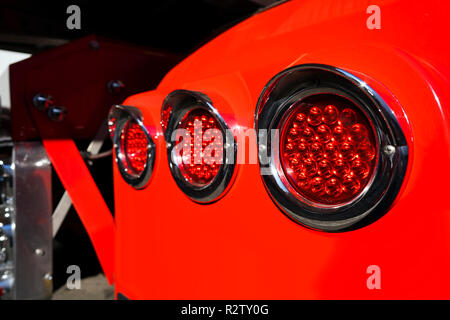 Line of rear round red marker lights with chrome rims on fender of red big rig semi truck shining on the sun Stock Photo