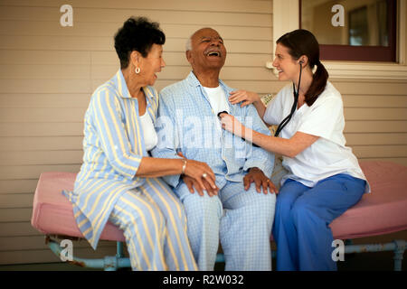 Young female nurse sitting with an elderly patient and his wife on their verandah. Stock Photo
