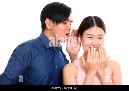 Studio shot of young Asian couple with man whispering to woman l Stock Photo