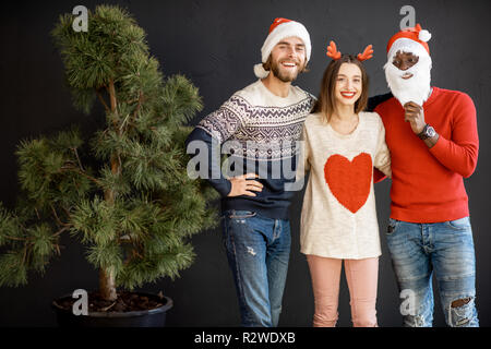 Young friends dressed in sweaters with New Year hats celebrating winter holidays together indoors Stock Photo