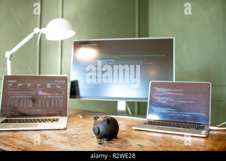 Black piggybank on the table with computers on the background Stock Photo