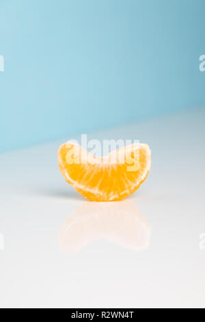 Wedge of tangerine on white and blue background. Minimalistic image of piece of orange fruit at sparse bright environment. Stock Photo