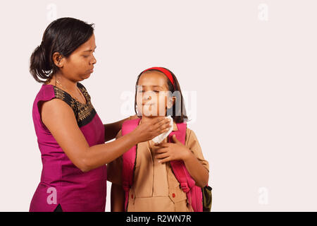 Mother cleans daughter's face with tissue. Daughter in school uniform. Pune, Maharashtra Stock Photo