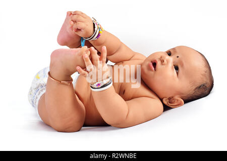 Cute baby sleeping on bed holding his feet and laughing, Pune, Maharashtra. Stock Photo