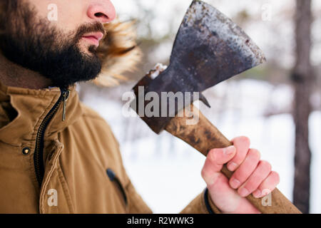 Beard and axe. Lumberjack standing with weathered rusty axe in his hand. Close view, unrecognizable man in forest. Neatly trimmed beard line. Trimmer or barber commercial. Stock Photo