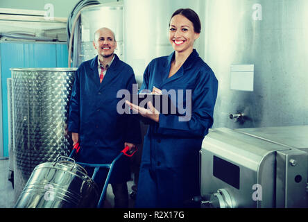Glad diligent positive female winery worker taking notes while male one working in fermentation section Stock Photo