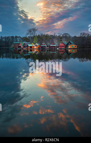 Tata, Hungary - Beautiful sunset over wooden fishing cottages on a small island at lake Derito (Derito to) in November with reflection Stock Photo