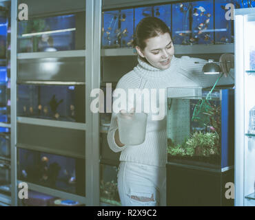 happy english girl holding aquarian net and water container next to aquarium with colorful fish in aquarium shop Stock Photo
