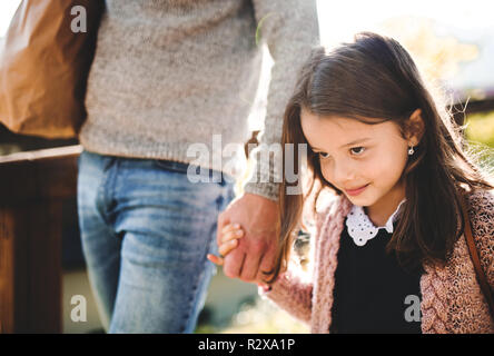 A small girl with unrecognizable father walking outdoors in park in autumn. Stock Photo