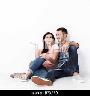 Happy young couple sitting on floor looking up while dreaming their new home and furnishing. Mock up for design. Stock Photo